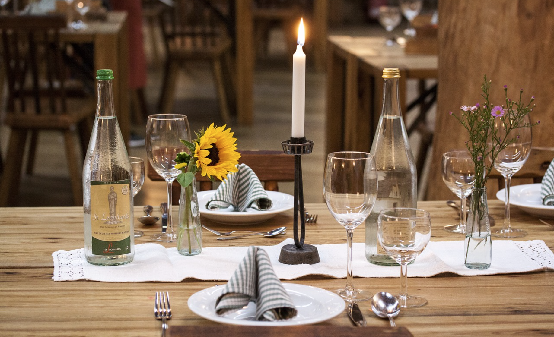 Bord dekket til måltid med duk, tallerkenes, bestikk, glass, flasker og blomster.